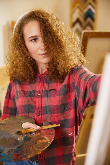 Beautiful girl listens to music via headphones and is drawing a painting with oils