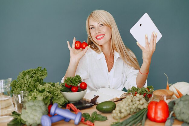 Beautiful girl make a salad. Sporty blonde in a kitchen. Woman writing recipe in notebook.