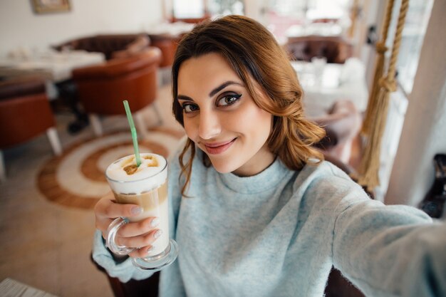 Красивая девушка делает автопортрет с кофе латте в кафе