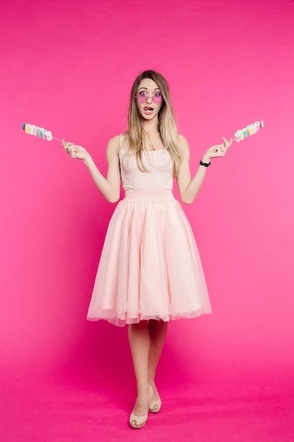 Free photo beautiful girl in pink like princes showing marshmallows on stick
