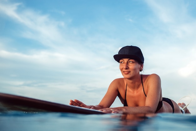 Beautiful girl posing sitting on a surfboard in the ocean