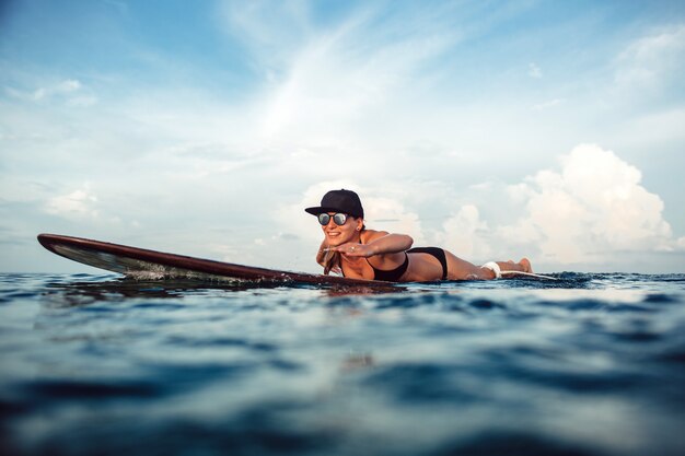 Beautiful girl posing sitting on a surfboard in the ocean