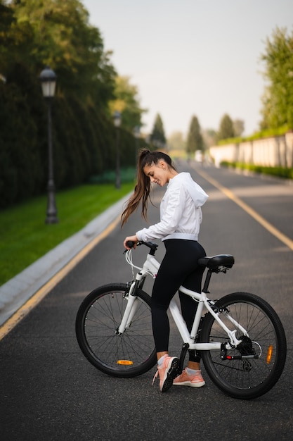 白い自転車でポーズをとる美しい少女。自然の中を歩きます。