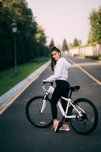 白い自転車でポーズをとる美しい少女。自然の中を歩きます。