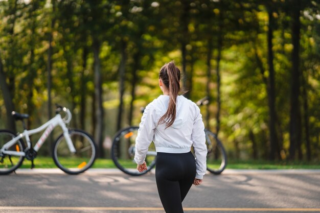 白い自転車でポーズをとる美しい少女。自然の中を歩きます。