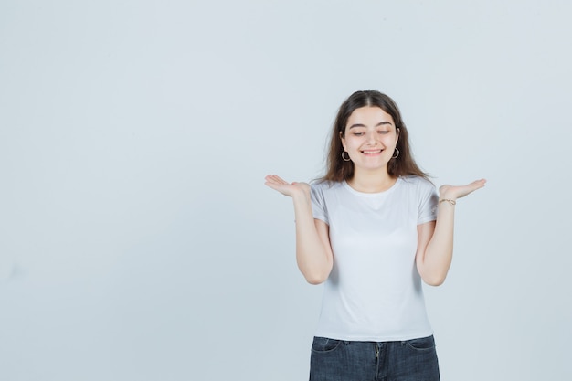 Bella ragazza che mostra gesto di benvenuto in t-shirt, jeans e sembra allegra. vista frontale.