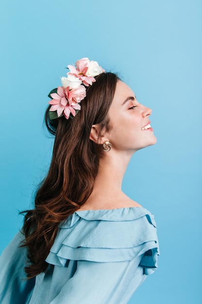 Bella ragazza sinceramente sorridente sulla parete isolata. modello in corona di fiori in posa per il ritratto di profilo.