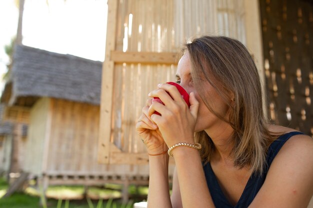 美しい少女がバンガローの近くに座ってコーヒーを飲みます。