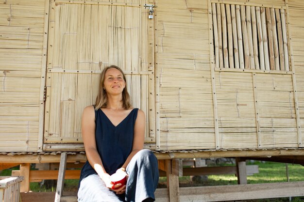 Beautiful girl sits near the bungalow and drinks coffee. 