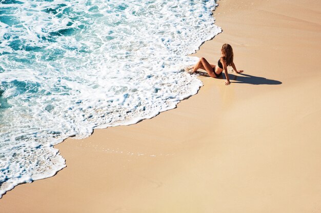 Beautiful girl sits on a wild beach. amazing view from the top.