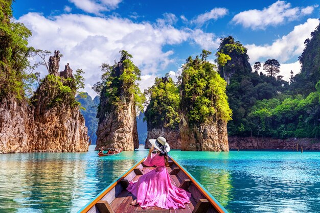 Beautiful girl sitting on the boat and looking to mountains in Ratchaprapha Dam at Khao Sok National Park, Surat Thani Province, Thailand.