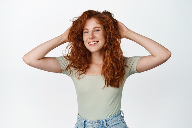 Beautiful girl smiles and looks happy resting with hands behind head lay back and watch something standing over white background Copy space