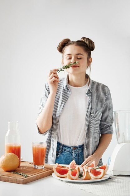 Beautiful girl smiling with closed eyes sniffing rosemary. Healthy diet fitness nutrition. Grapefruit detox smoothie.