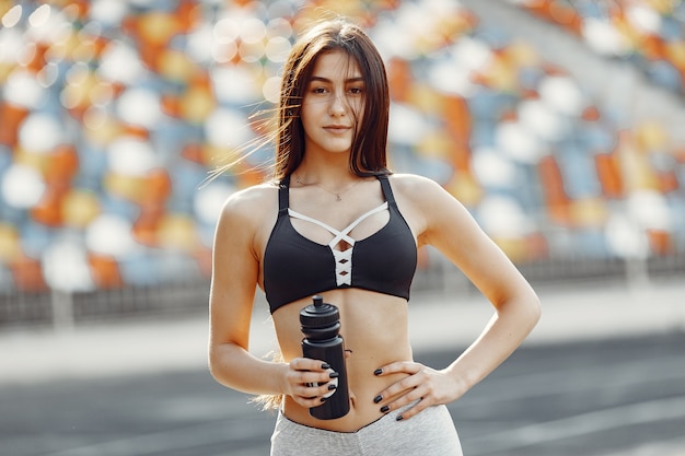 Beautiful girl at the stadium. Sports girl in a sportswear. Woman with bottle of water.