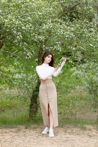 Beautiful girl standing in blooming park holding tree branch looking forward admiring