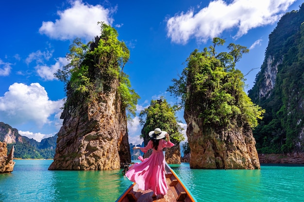 Красивая девушка стоит на лодке и смотрит на горы в плотине Ратчапрафа в национальном парке Као Сок, провинция Сураттани, Таиланд.