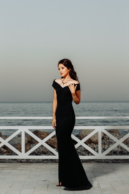 Beautiful girl standing in near the seaside in long black dress during daytime