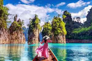 Бесплатное фото Красивая девушка стоит на лодке и смотрит на горы в плотине ратчапрафа в национальном парке као сок, провинция сураттани, таиланд.