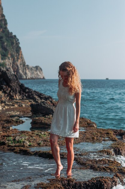 Beautiful girl standing in white dress in seashore during daytime .