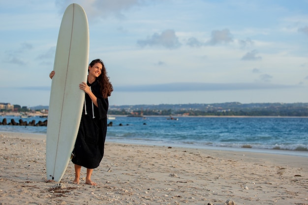 Beautiful girl stands on the beach with a surfboard.