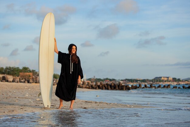 Beautiful girl stands on the beach with a surfboard.