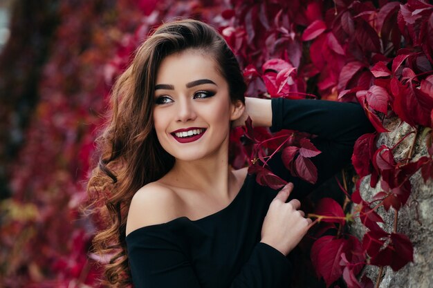 Красивая девушка стоит возле стены с листьями