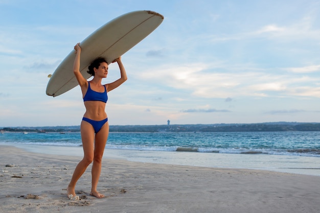 Бесплатное фото Красивая девушка стоит на пляже с доской для серфинга.