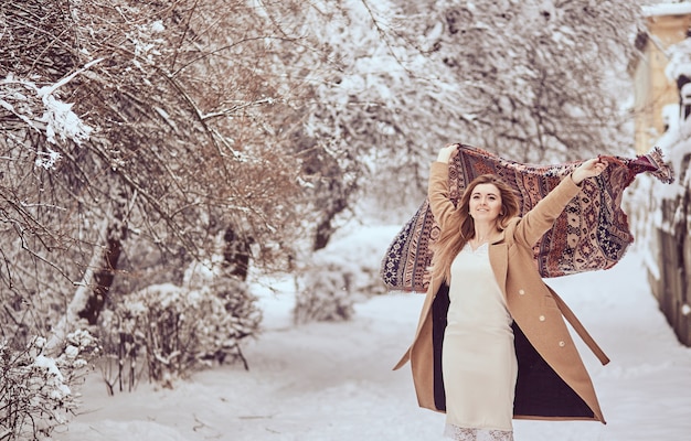 Beautiful girl stands with scarf fluttering in the wind in a winter park