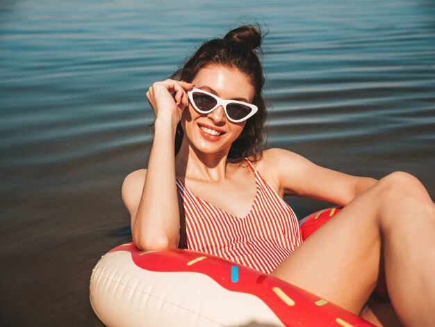 Beautiful girl in swimwear floating with an inflatable donut on the sea