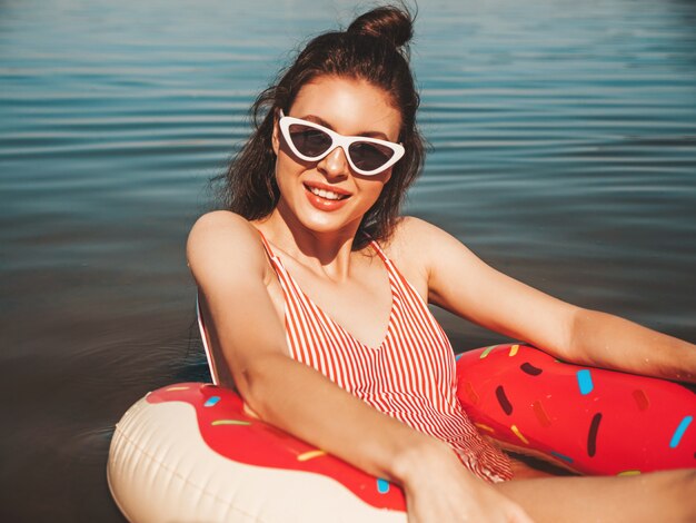 Красивая девушка в купальных костюмах плавает с надувным пончиком на море