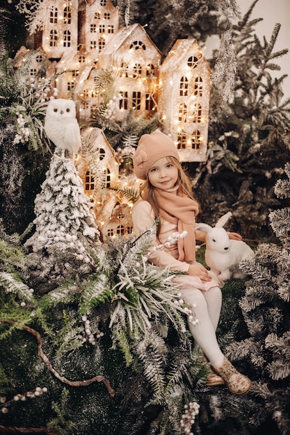 아름다운 소녀는 눈과 조명 아래에서 많은 나무가있는 크리스마스 장식에서 사진을 찍습니다.