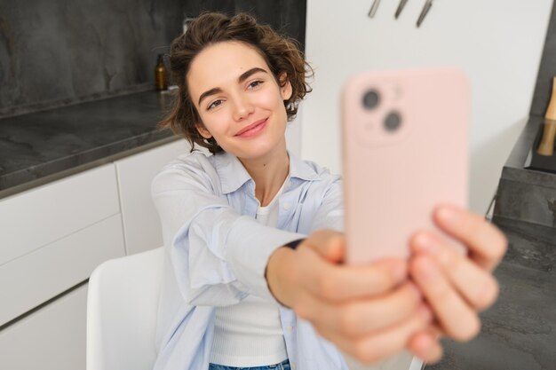 아름다운 소녀는 부에서 스마트폰으로 셀피를 찍고 집에서 휴대전화로 사진을 찍습니다.