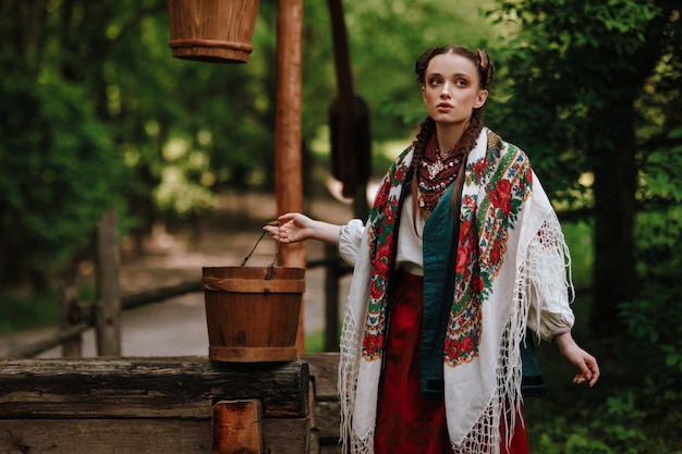 Foto gratuita bella ragazza in un tradizionale abito etnico pone al pozzo