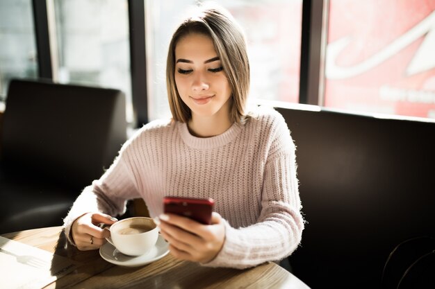 Красивая девушка с помощью своего мобильного телефона в кафе во время обеда с перерывом на кофе ежедневно