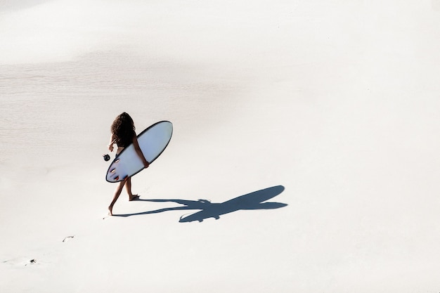 무료 사진 아름 다운 소녀는 야생 해변에서 서핑 보드와 함께 산책. 정상에서 놀라운 전망.