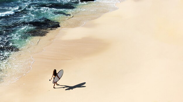 아름 다운 소녀는 야생 해변에서 서핑 보드와 함께 산책. 정상에서 놀라운 전망.