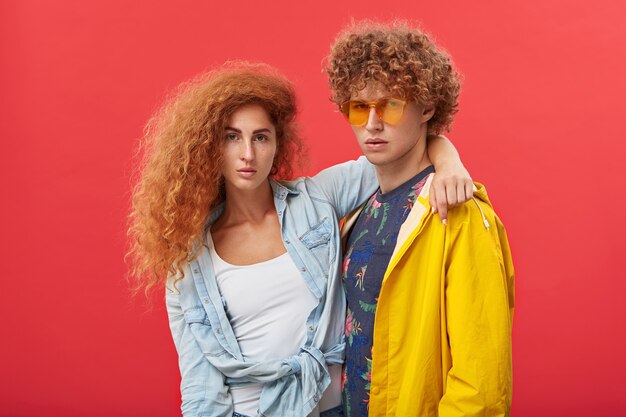 Beautiful girl with clean freckled skin and ginger voluminous hair embracing a red-haired man in eyewear