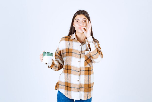 Beautiful girl with cup of coffee standing and gesturing delicious sign. 