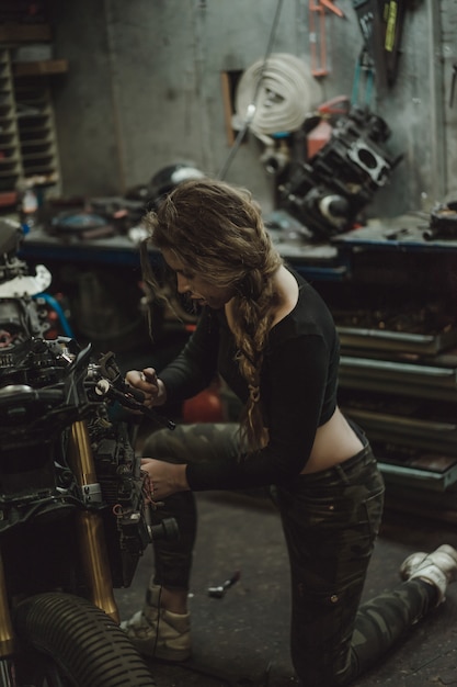 Foto gratuita bella ragazza con i capelli lunghi nel garage di riparare una moto