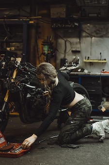 Красивая девушка с длинными волосами в гараже, ремонт мотоцикла