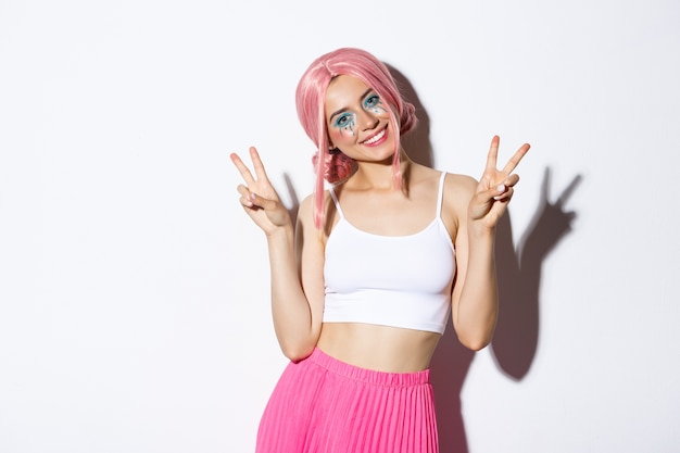 Free photo beautiful girl with lovely smile, showing peace signs, wearing pink wig and halloween makeup, standing.