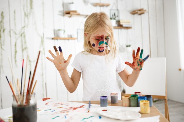 Beautiful girl with painted face wearing white t-shirt drawing with her hands on white sheets of paper