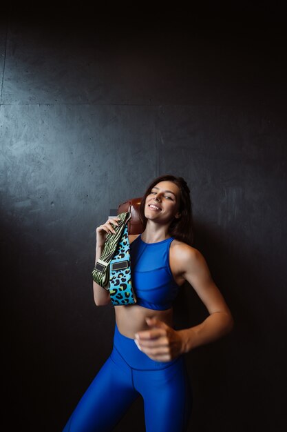 Beautiful girl with a sports figure stands on a dark wall and pose