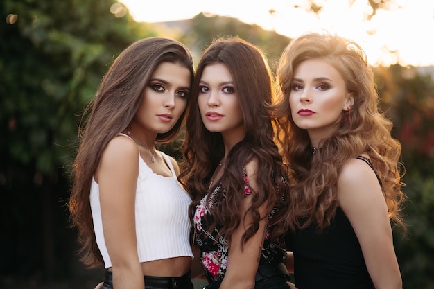 Foto gratuita belle amiche in uno sfondo della città con un bel trucco con abiti eleganti aperti concetto di un ritratto di tre belle ragazze