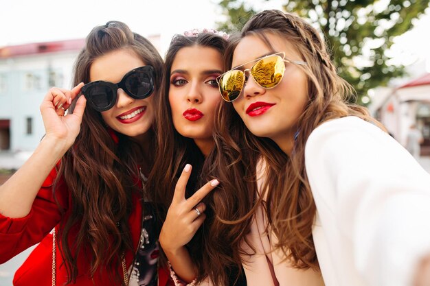 Beautiful girlfriends in sunglasses showing peace signs at camera with smile.