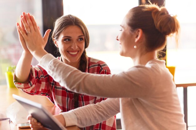 beautiful girls giving highfive while spending free time in cafe talking about every day things.