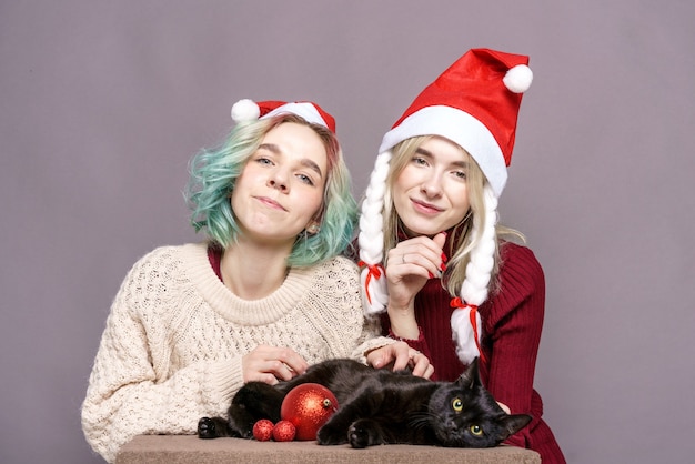 セーターを着た美しい女の子が両方の帽子の黒い猫に触れますクリスマスサンタクロースの若い女性...