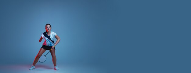 네온 불빛에 파란색 배경에 고립 배드민턴에서 연습하는 아름 다운 핸디캡 여자. 포용적인 사람, 다양성 및 평등의 라이프 스타일. 스포츠, 활동 및 움직임. 광고 Copyspace입니다. 전단