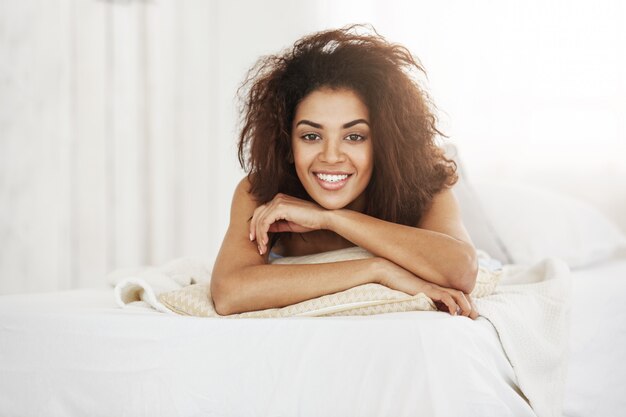 Beautiful happy african woman lying on pillow at home smiling.