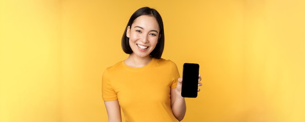 Красивая счастливая азиатская девушка показывает приложение экрана мобильного телефона на гаджете смартфона, стоящем над